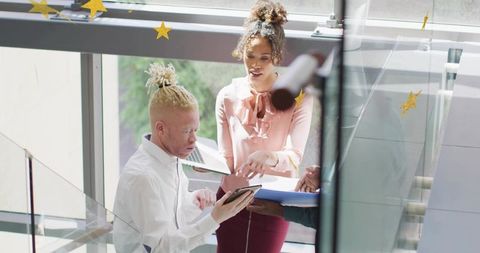Young professionals collaborating with tablet and laptop on modern glass stairwell