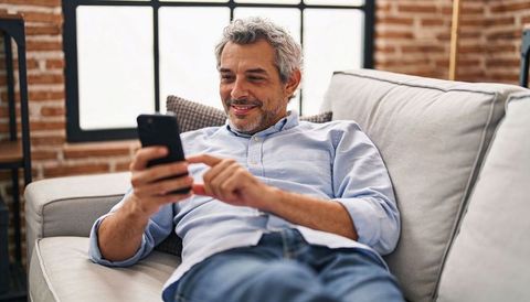 Middle-aged man reclining on sofa using smartphone, casual home relaxation and messaging