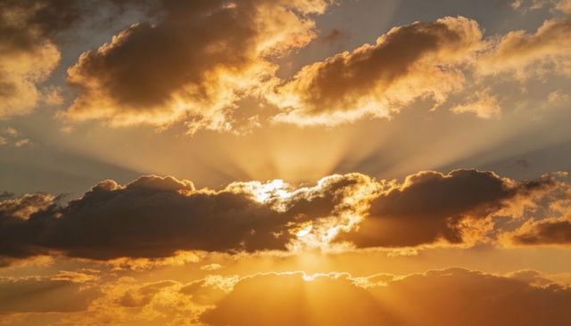 Sun glowing behind dense cloud band creating dramatic golden crepuscular rays at sunset