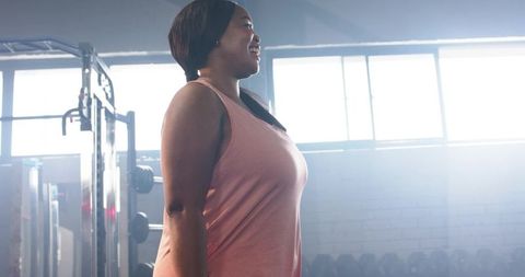 African american woman standing with dumbbells in backlit gym for fitness confidence
