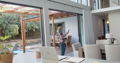 Man Using Smartphone in Modern Open-Concept Home with view of Pool and Deck