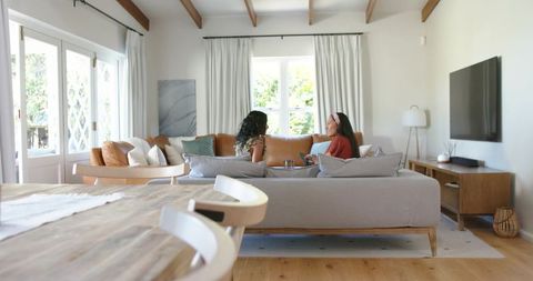 Sunlit contemporary living room: diverse friends chatting on modern gray sofa