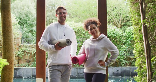 Portrait of biracial couple standing together holding yoga mats at vacation home. active and healthy lifestyle during vacation concept