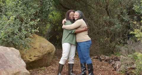 Friends hugging and smiling on forest trail wearing rubber boots embracing nature