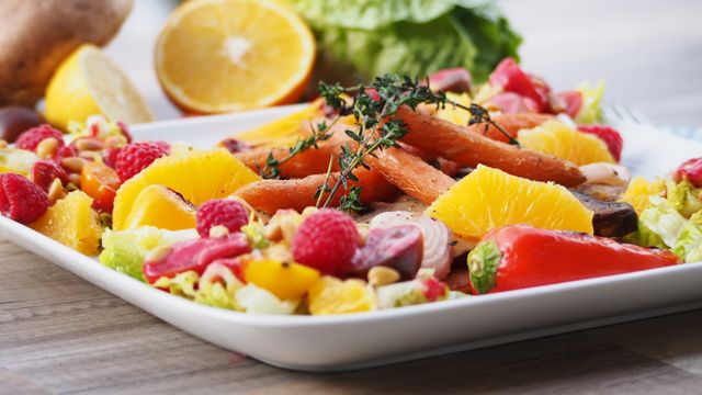 Fresh colorful salad featuring a mix of fruits and vegetables such as oranges, raspberries, carrots, and bell peppers, arranged on a plate with fresh herbs on top. Ideal for use in content promoting healthy eating, diet recipes, culinary presentations, food blogs, and nutrition-related articles.