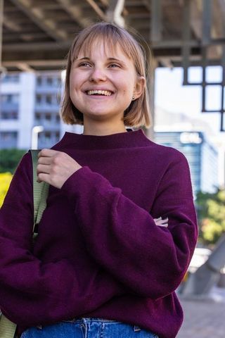 Young woman smiling under urban canopy wearing burgundy sweater, carrying green-strap bag