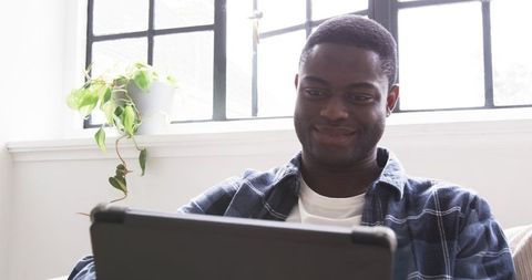 Man Relaxing on Sofa with Tablet Near Window Plant