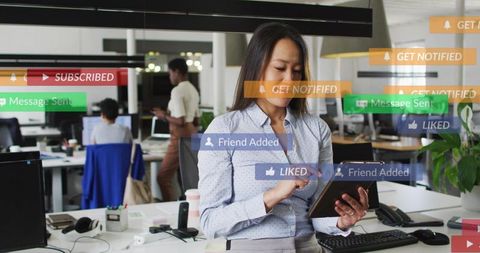 Korean woman tapping tablet in modern open office with social media notifications