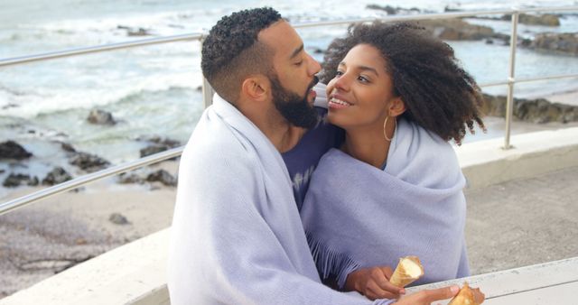 Romantic diverse couple with blankets on backs and ice creams talking and embracing on sunny beach. Summer, vacation, romance, love, relationship, free time and lifestyle, unaltered.