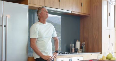 Relaxed middle-aged man breathing deeply in modern kitchen enjoying calm morning routine