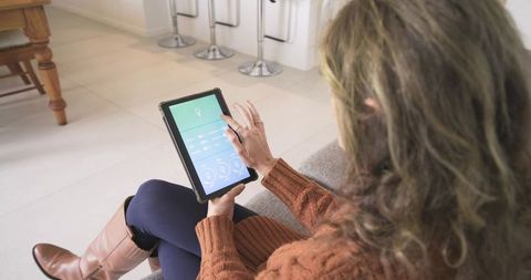 Woman Using Tablet for Smart Home Control While Relaxing in Stylish Living Room