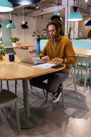 African american man working on laptop in modern coworking cafe reviewing charts