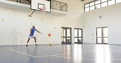 Dribbling basketball player practicing on sunlit indoor court with empty space for copy