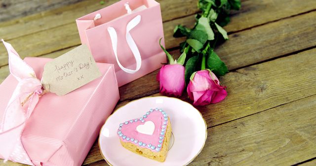 A Valentine's Day themed setup features a heart-shaped cookie on a plate, pink roses, and a gift bag with a card, all on a wooden surface. The arrangement captures the essence of the romantic holiday with its thoughtful gifts and sweet treats.