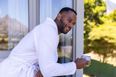 Mature african american man enjoying morning coffee on balcony in white bathrobe
