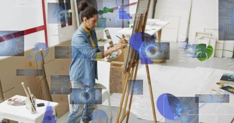 Mature artist painting on easel, mixing paints in sunlit studio with holographic overlays