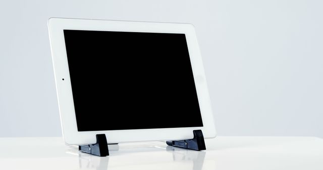 White tablet with black blank screen resting on black stand over solid white surface, against plain white background. Perfect for technology presentations, mock-ups, and web design showcases.