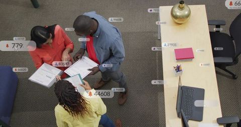 Collaborative team reviewing documents at office desk with laptop, brainstorming together