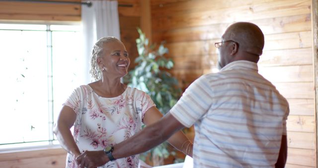 Happy senior african american couple holding hands and talking on sunny living room. Retirement, summer, relaxation, togetherness, domestic life and senior lifestyle, unaltered.