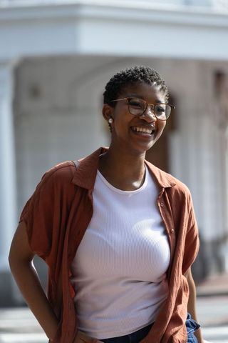 African american woman smiling on city sidewalk wearing rust-brown shirt, eyeglasses