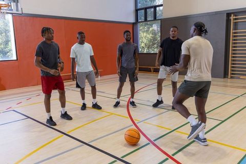 Five african american men practicing basketball drills and defense in indoor gymnasium