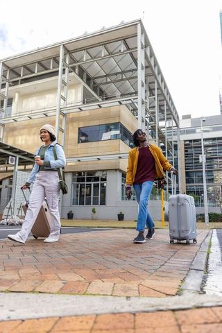 Young travelers walking through urban plaza pulling rolling suitcases and holding coffee