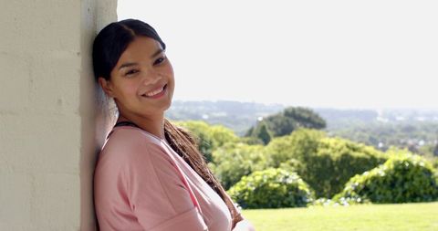 Smiling woman on sunny porch relaxing against white column