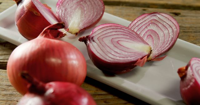 Freshly sliced red onions placed on rectangular white plate on wooden table. great for use in culinary blogs, cooking tutorials, recipe illustrations, grocery advertisements, and food-related content.