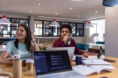 College students collaborating at communal study table with laptops, notebooks, coffee