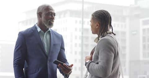 Senior black executive mentoring younger colleague discussing work in glass office lobby