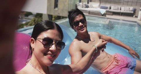 Couple taking selfie on pool float, smiling sunglasses swimwear, summer social media content