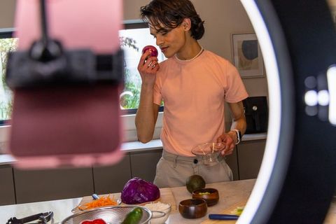Young Asian man preparing colorful meal at kitchen island under ring light for content
