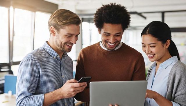 Multicultural team collaborating over laptop and smartphone in bright modern office