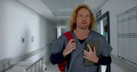 Male Medical Intern Walking Hospital Corridor for Healthcare Work