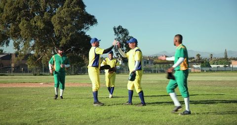 Baseball teammates celebrating with high-five on sunny field in yellow and green uniforms
