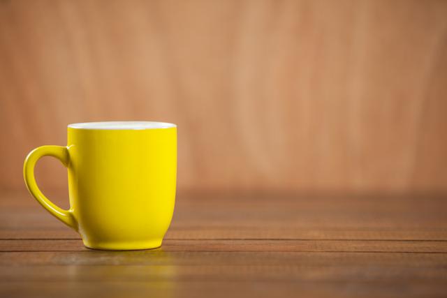 Yellow coffee mug on wooden table over brown background