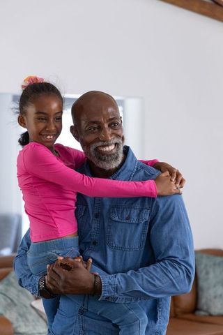 African american grandfather holding smiling granddaughter in cozy home embrace