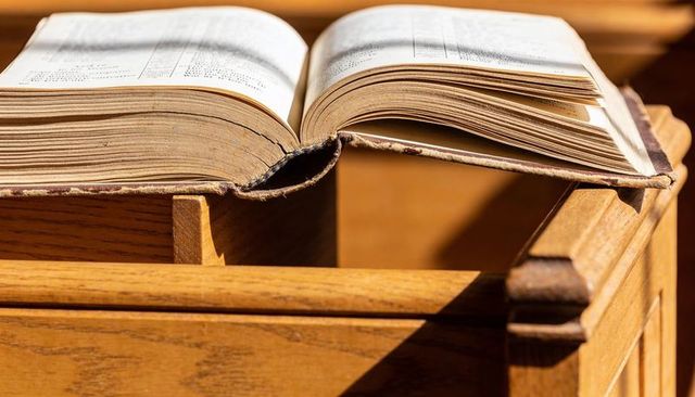 Antique hardcover book resting on sunlit wooden lectern, yellowed pages and worn spine