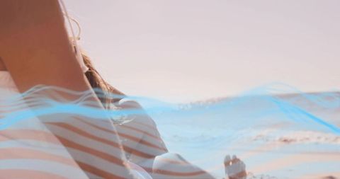Sunlit beach relaxation woman lying on striped towel at shoreline with soft blue overlay
