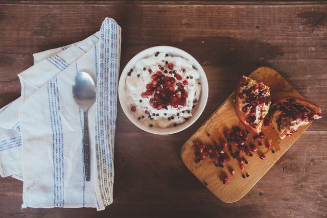 Health-conscious individuals may find this image perfect for representing a nutritious morning meal. The setup shows a rustic scene with a bowl of creamy yogurt topped with pomegranate seeds and dark chocolate chips on a wooden table, along with a spoon and cloth napkin, evoking a homey, farm-to-table aesthetic. Ideal for promoting food blogs, healthy eating, Instagram posts, or cookbooks featuring easy healthy recipes.