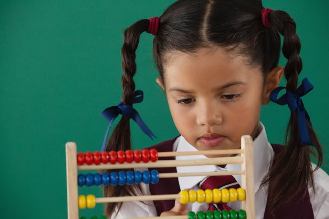 Schoolgirl in uniform using an abacus against a green chalkboard background. Ideal for educational resources, school posters, math tutorials, or articles on child development and education.