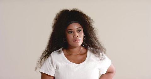 Confident african american woman wearing white tee and headband posing in timeless studio