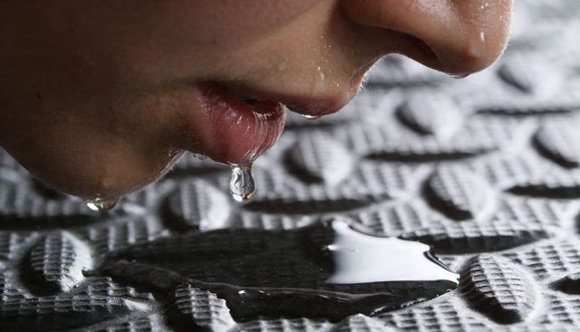 Lower face leaning over textured mat with lip droplet and puddle macro details