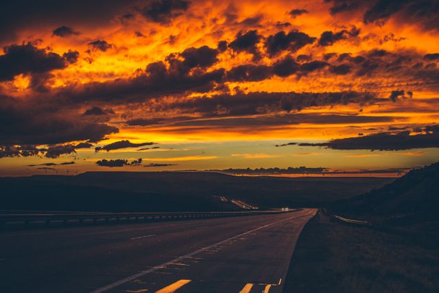 Capturing a dramatic and breathtaking sunset over an empty highway, this scene is perfect for travel advertisements, landscape photography showcases, and websites specializing in environmental beauty. The dramatic clouds enhance the sky's rich colors, invoking feelings of awe and wanderlust.