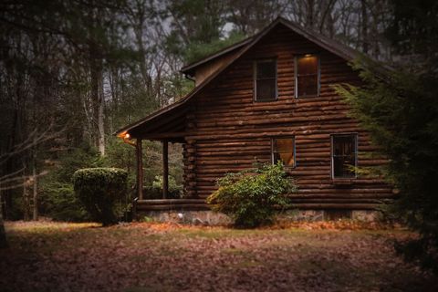 Cozy rustic log cabin at dusk in forest with warm window light and autumn foliage