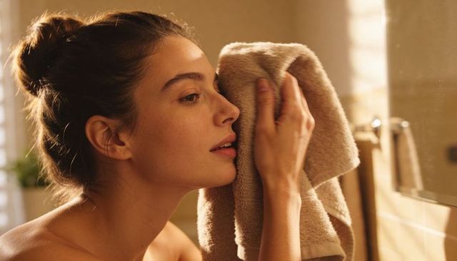 Woman drying face with beige towel in warm bathroom light close-up profile soft portrait