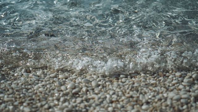 Lapping foam washing smooth white pebbles along turquoise shallow shore, minimalist texture
