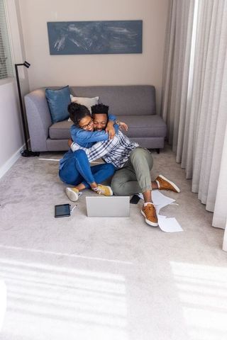 Couple hugging on carpet while working from home with laptop and papers