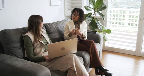 Middle-aged colleagues collaborating on laptop while sharing coffee on sofa