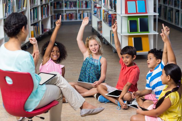 Children enthusiastically raising hands in a library during a class session with a female teacher. This image can be used for educational materials, school brochures, websites promoting literacy and learning, or articles about interactive teaching methods and classroom engagement.
